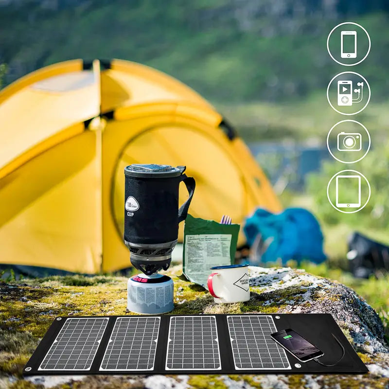 Portable Solar Charger on the ground with camping gear near a yellow tent, perfect for hiking and outdoor activities.